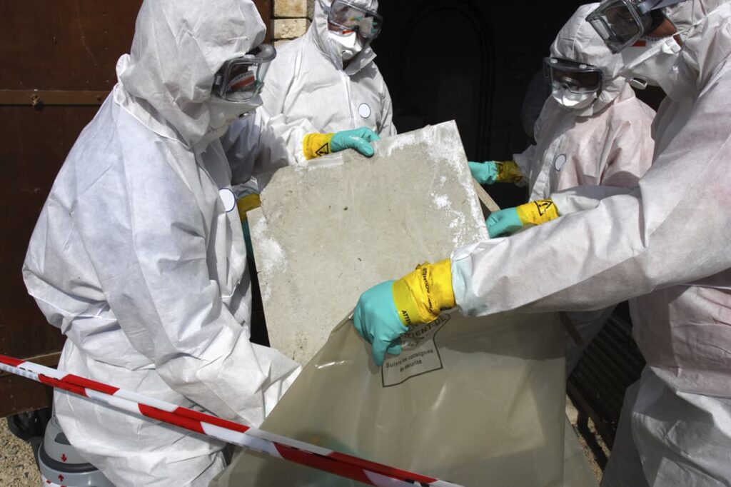 Workers in hazmat suits removing ceiling panels with asbestos