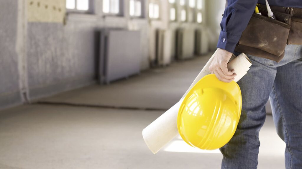 I man carrying construction plans and a hardhat in a building location