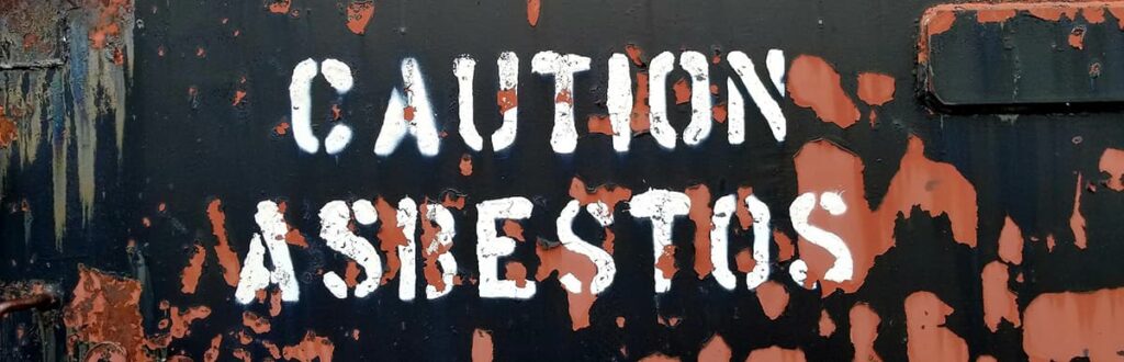 Wall with the words "caution asbestos" spray painted on it