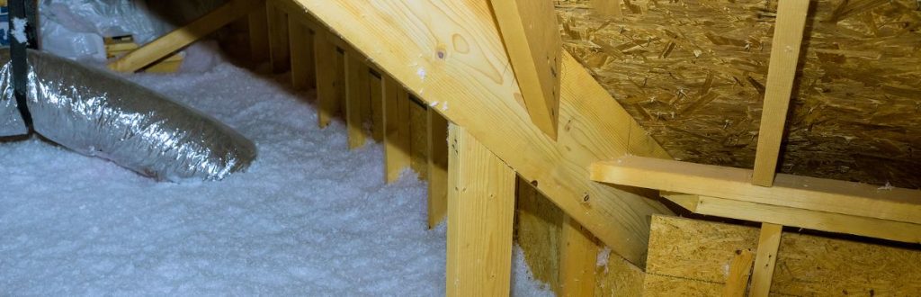 HVAC ducting surrounded by white, fluffy material in a wooden attic environment.