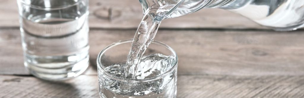 Clean drinking water being poured from pitcher to glass.