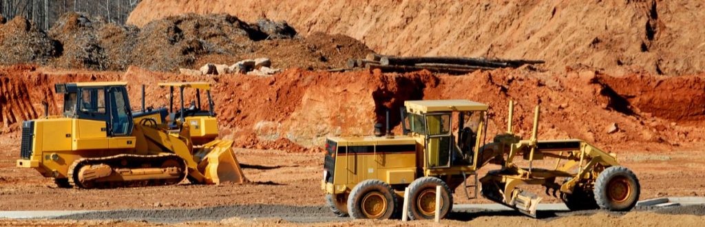 Yellow construction vehicles are parked on a red dirt desert construction site.